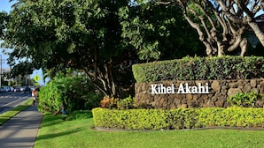 A sign with "Kihei Akahi" written on a stone wall, surrounded by well-maintained grass and bushes.