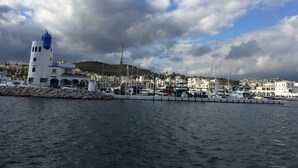 A coastal marina with boats, a lighthouse, and a town in the background. - PENTHOUSE WITH AC, SEA VIEW, PANORAMIC TERRACE OF 100 M2 LOUNGE TRANSATS (ALCORRIN - PUERTO LA DUQUESA - COSTA DEL SOL)