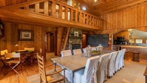 Interior de una cabaña de madera con comedor, cocina y una chimenea de piedra.