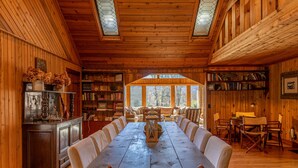 Un gran comedor de madera con sillas, rodeado de estanterías y vistas al exterior.