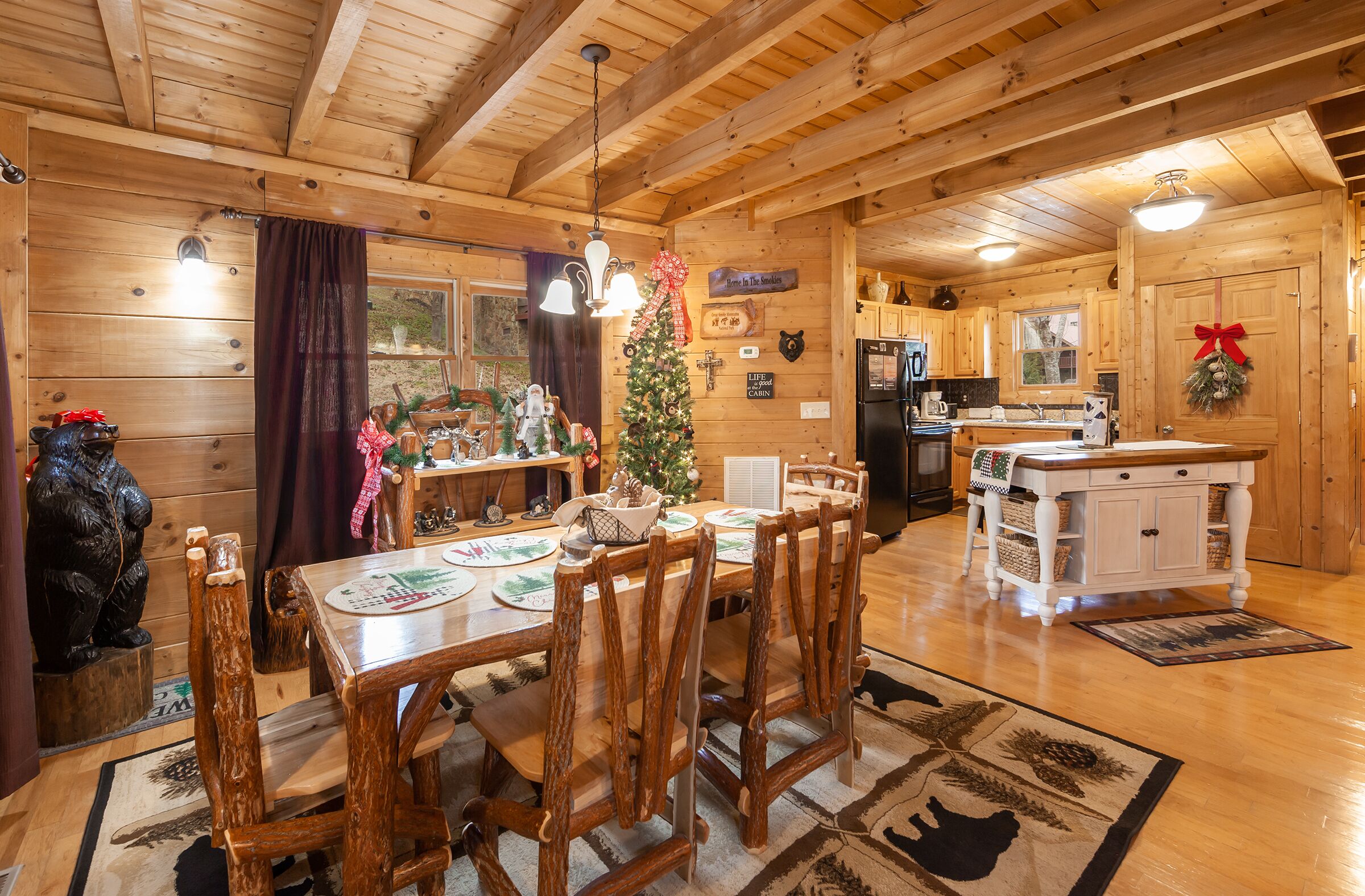 Interior de una cabaña de madera con comedor, cocina y un árbol de Navidad.