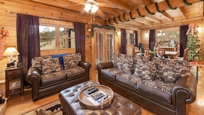 A cozy log cabin interior with two leather sofas, a wooden coffee table, and a ceiling fan. - Spacious 2 BR w/Hot Tub | Pool Table | Wi-Fi (Sevierville)