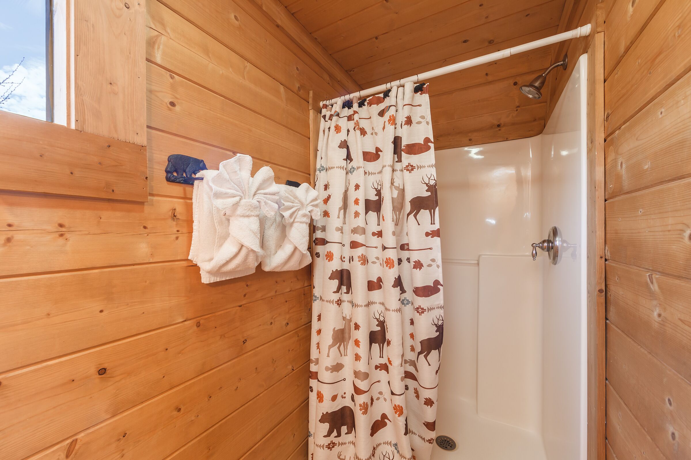 A wooden cabin bathroom with a shower curtain featuring animal prints, a white bathtub, and a towel rack with a white towel.