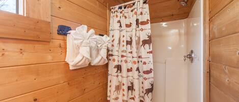 A wooden cabin bathroom with a shower curtain featuring animal prints, a white bathtub, and a towel rack with a white towel.