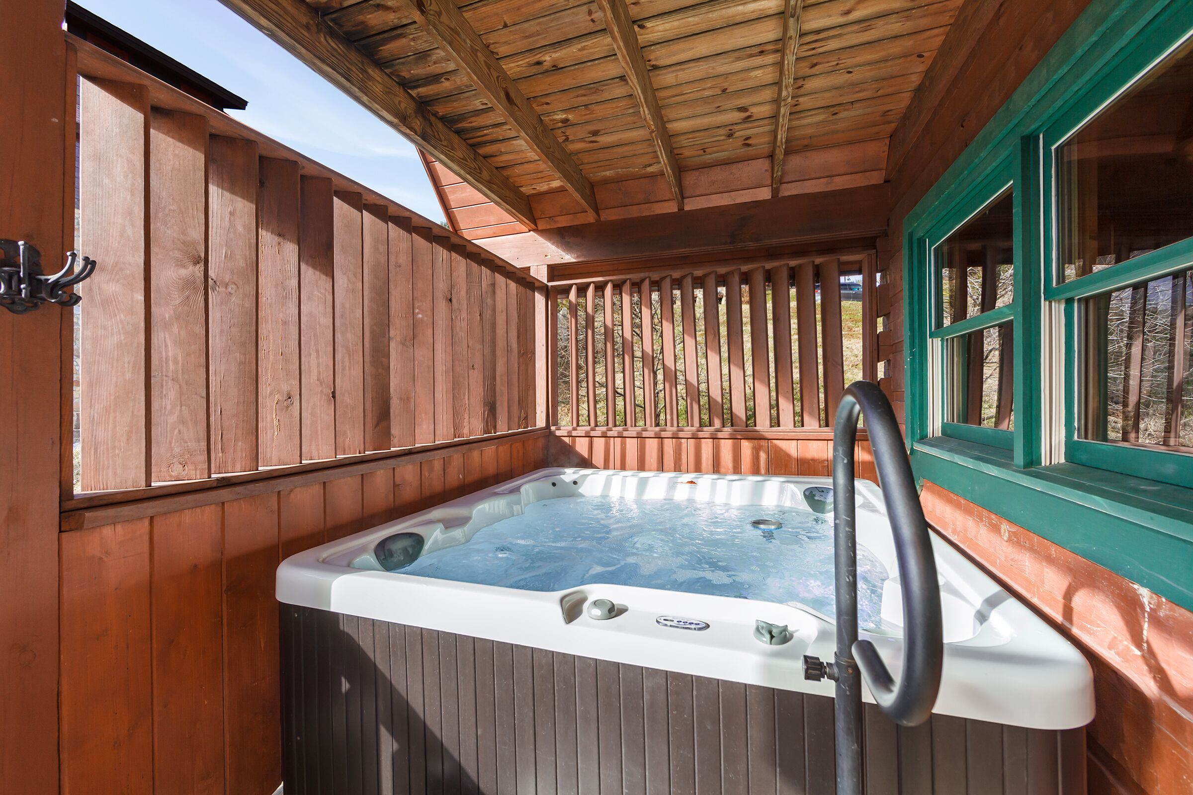 Eine Holzterrasse mit Whirlpool, Metallgeländer und einem Fenster mit grüner Verzierung.