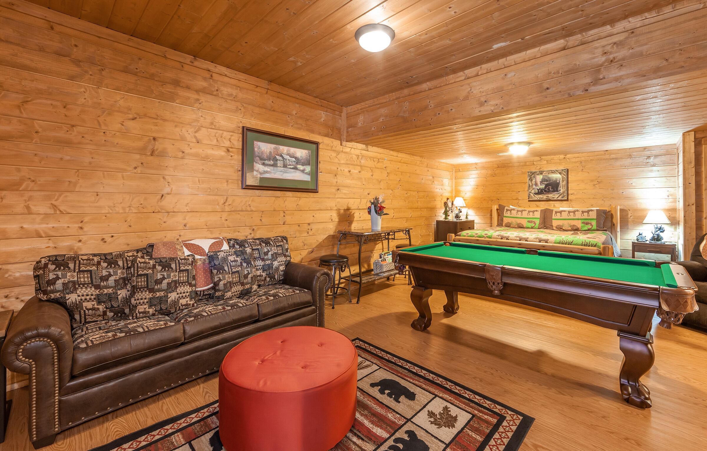 Una habitación acogedora con paredes de madera, una mesa de billar, un sofá y un pouf rojo.