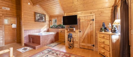 A log cabin interior with a wooden ceiling, a television, a fireplace, and a wooden cabinet.