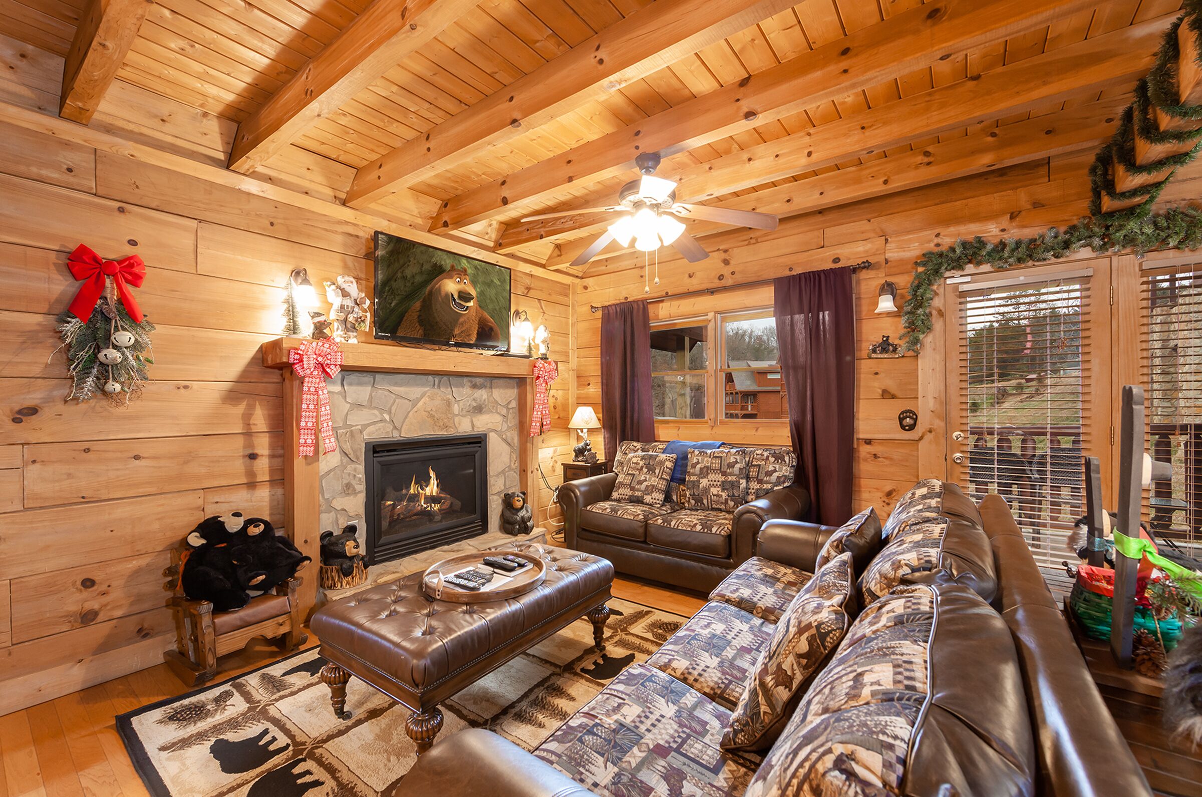 A cozy log cabin interior with a fireplace, leather furniture, and festive decorations.