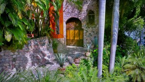 A stone building with a wooden door, surrounded by lush tropical vegetation.