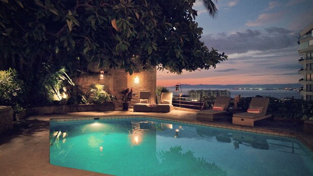 A pool area with lounge chairs and a view of the sea at dusk.