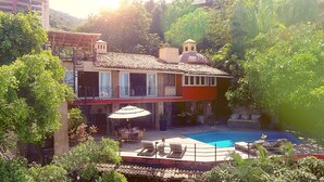 A two-story building with a swimming pool, outdoor seating, and lush greenery.