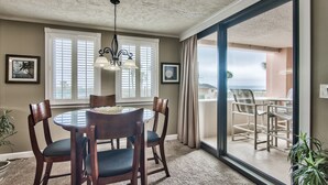 A dining area with a round table and four chairs, a chandelier, and a view through a glass door to an outdoor seating area.