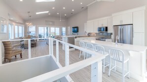 Une cuisine spacieuse avec des meubles blancs, un îlot central et un coin repas doté de chaises blanches.
