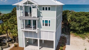 Une maison à plusieurs étages située en bord de mer, dotée d’un balcon au deuxième étage, d’un porche couvert et offrant une vue sur l’océan.