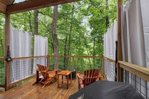 Terraza de madera con sillas Adirondack, una mesa y una parrilla, con vista a un área boscosa.