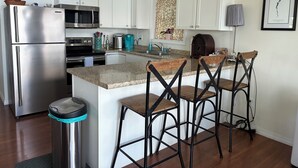 A kitchen with white cabinets, stainless steel appliances, a granite countertop, and bar stools. - Beautiful  camp nestled at the end of a dead end road. (Swanton)