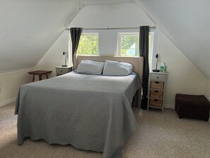 Un dormitorio con cama, mesitas de noche, una ventana y un taburete pequeño.