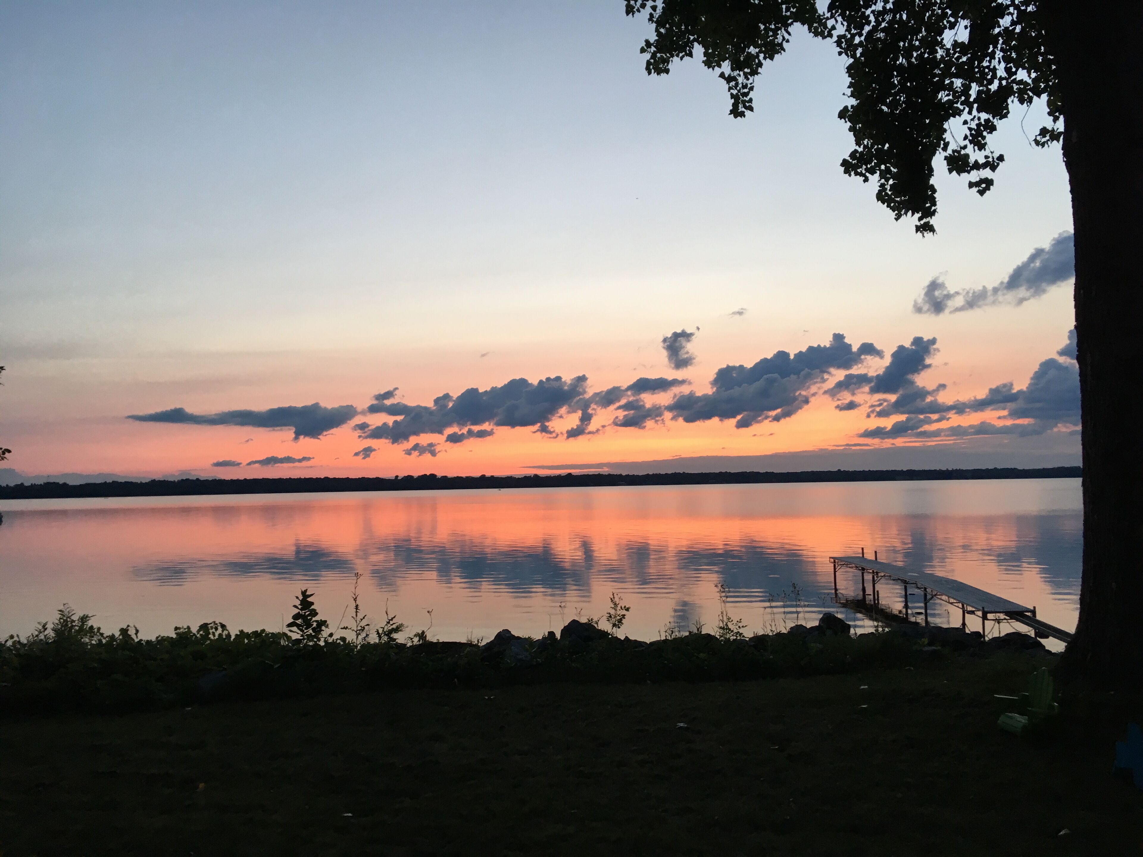 Ein ruhiger See bei Sonnenuntergang, mit einer anlegenden Mole, die ins Wasser führt.