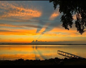 Un atardecer sobre una masa de agua tranquila, con un muelle que se adentra en el agua.