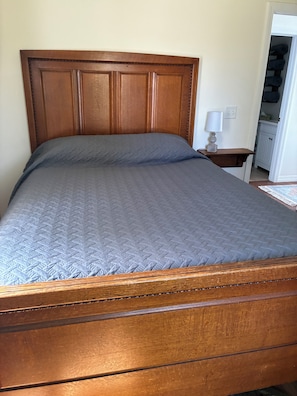 A wooden bed with a headboard, a bedside table with a lamp, and a closet with hanging clothes.