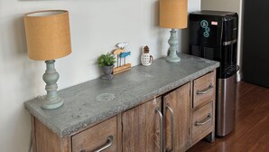 A kitchenette with a coffee maker, a framed picture, and a welcome sign.