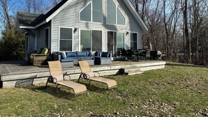 A house with a large deck, outdoor seating, and a view of the surrounding trees.