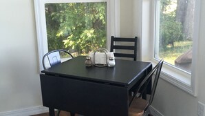 A dining table with chairs, salt and pepper shakers, and a window with a view of greenery. - Beautiful  camp nestled at the end of a dead end road. (Swanton)