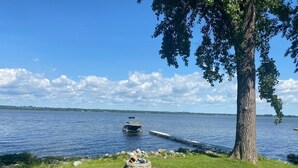 A lakeside scene with a boat dock, a tree, and a grassy area with a stone structure.