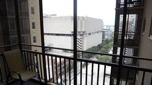 Een balkon met een stoel, uitzicht op een stadsgezicht met gebouwen, en een vloerkleed met een patroon.