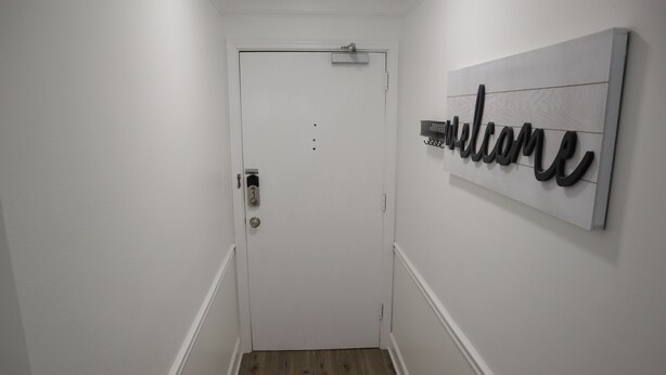 Een gang met een witte deur, een welkomstbord en een houten vloer.