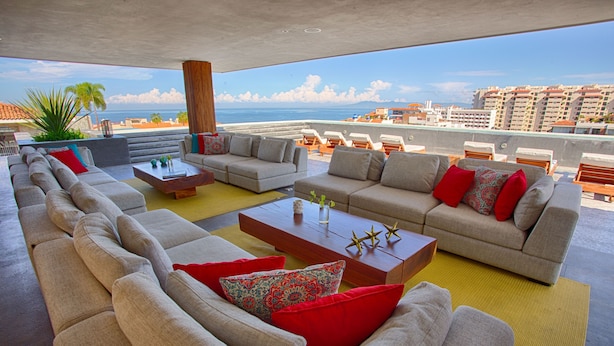 A spacious outdoor seating area with multiple sofas and a coffee table, overlooking a cityscape and the ocean. - Designer 2BR w/ Balcony & Pool in Romantic Zone (Puerto Vallarta)
