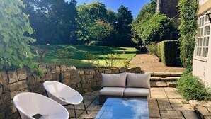 Un espace patio aménagé avec un ensemble de canapés, deux chaises blanches et une table à plateau en verre.