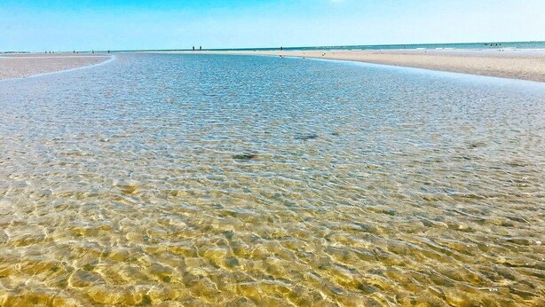 Une plage avec une eau claire et peu profonde et une vaste étendue de sable.