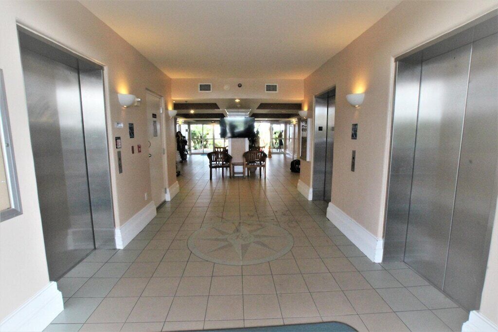 Un corridoio d'albergo con ascensori, una zona relax centrale e un pavimento piastrellato.
