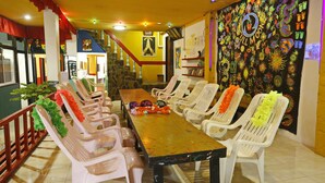 A dining area with a long table and white plastic chairs, decorated with colorful leis. - Om Ganesh Hostel - Adults Only (Ko Pha-ngan)