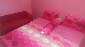 A small, pink-themed bedroom with a single bed, a red bench, and a patterned bedspread. - Om Ganesh Hostel - Adults Only (Ko Pha-ngan)