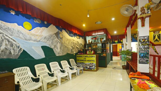 A hostel reception area with a mural of mountains, a welcome sign, white plastic chairs, and a counter with various items. - Om Ganesh Hostel - Adults Only (Ko Pha-ngan)