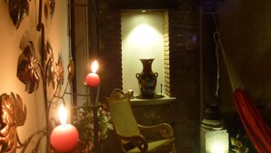 A dimly lit room with a stone wall, a wooden rocking chair, and a decorative metal wall piece. - Apartamentos los Nazarenos PRIVATE APT 1 - heated swimming pool, jacuzzi and gym (Antigua Guatemala)
