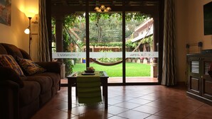 A living room with a sofa, a table with a green tablecloth, and a view through a glass door to an outdoor area with a hammock and greenery. - Apartamentos los Nazarenos PRIVATE APT 1 - heated swimming pool, jacuzzi and gym (Antigua Guatemala)