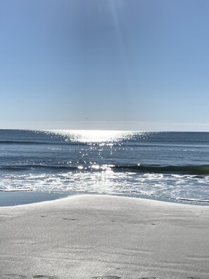 Ein Strand mit blauem Himmel und Sonnenlicht, das sich im Wasser spiegelt.