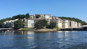 Un hôtel à plusieurs étages, doté de balcons donnant sur un plan d’eau et entouré de verdure.