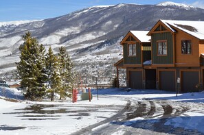 Une maison en bois à deux étages, dotée d’un garage, entourée d’un paysage enneigé et de montagnes.
