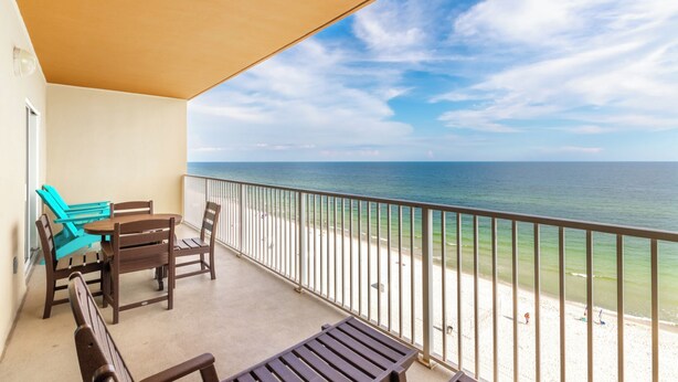 A balcony with a view of the ocean, a table with chairs, and a beach in the background.