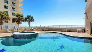 A swimming pool with a circular hot tub, lounge chairs, and palm trees.