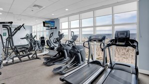 A gym with treadmills, ellipticals, and a TV screen.