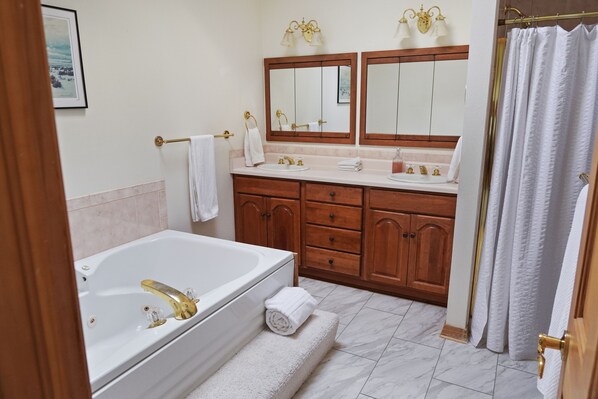 A bathroom with a bathtub, double sinks, wooden cabinets, and a large mirror.