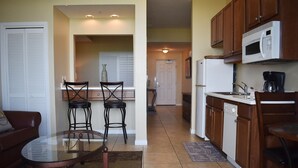 A compact kitchen with a dining area, featuring a refrigerator, microwave, and a small sink. - Destin West Beach Resort Villa Studio (Fort Walton Beach)