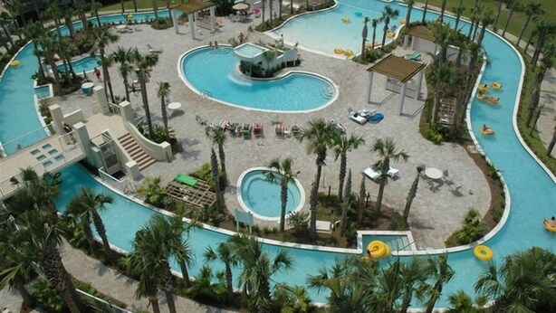 A large, winding pool with multiple sections and palm trees. There are lounge chairs and umbrellas around the pool area. - Destin West Beach Resort Villa Studio (Fort Walton Beach)