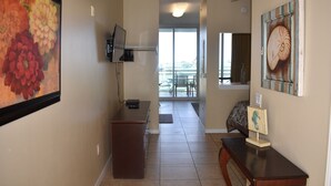 A hallway with a flat-screen TV mounted on the wall, a wooden bench, and a small table with a decorative item. - Destin West Beach Resort Villa Studio (Fort Walton Beach)