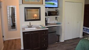 A compact kitchen with a sink, microwave, and a small refrigerator. There is a framed picture above the mirror and a surfboard-shaped sign on the wall. -  Fresh & Clean, Air Conditioned Second Floor Condo in Princeville  (Princeville)